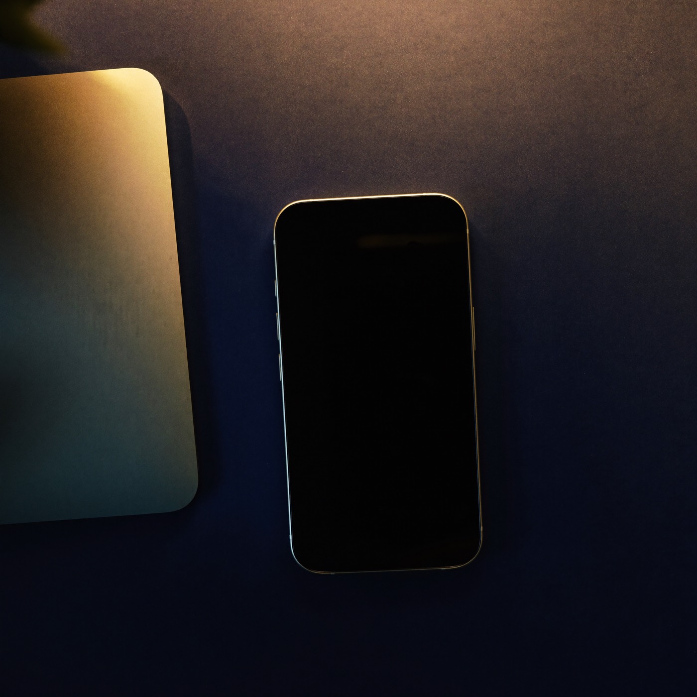 Smartphone and laptop on a dark desk with golden light
